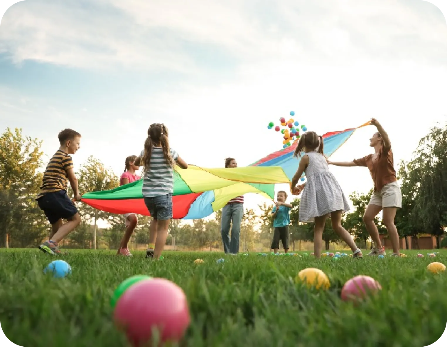 Niños y niñas jugando con un paracaídas de colores en un parque
